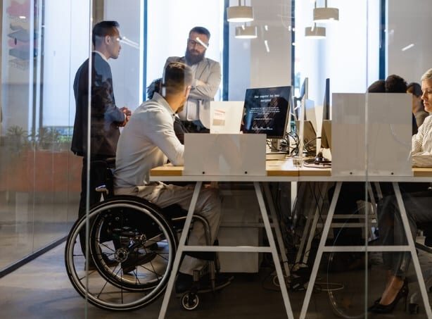 Employees in conference room working together discussing accessibility questions, one employee in wheelchair