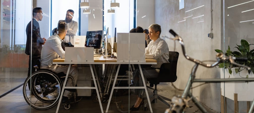 accessibility-questions-answered-blog-cover Employees in conference room working together, one employee in wheelcharir