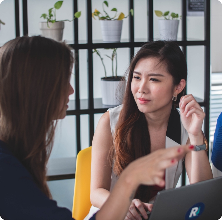 Two young women, creative professionals, in conversation at office discussing talent benefits