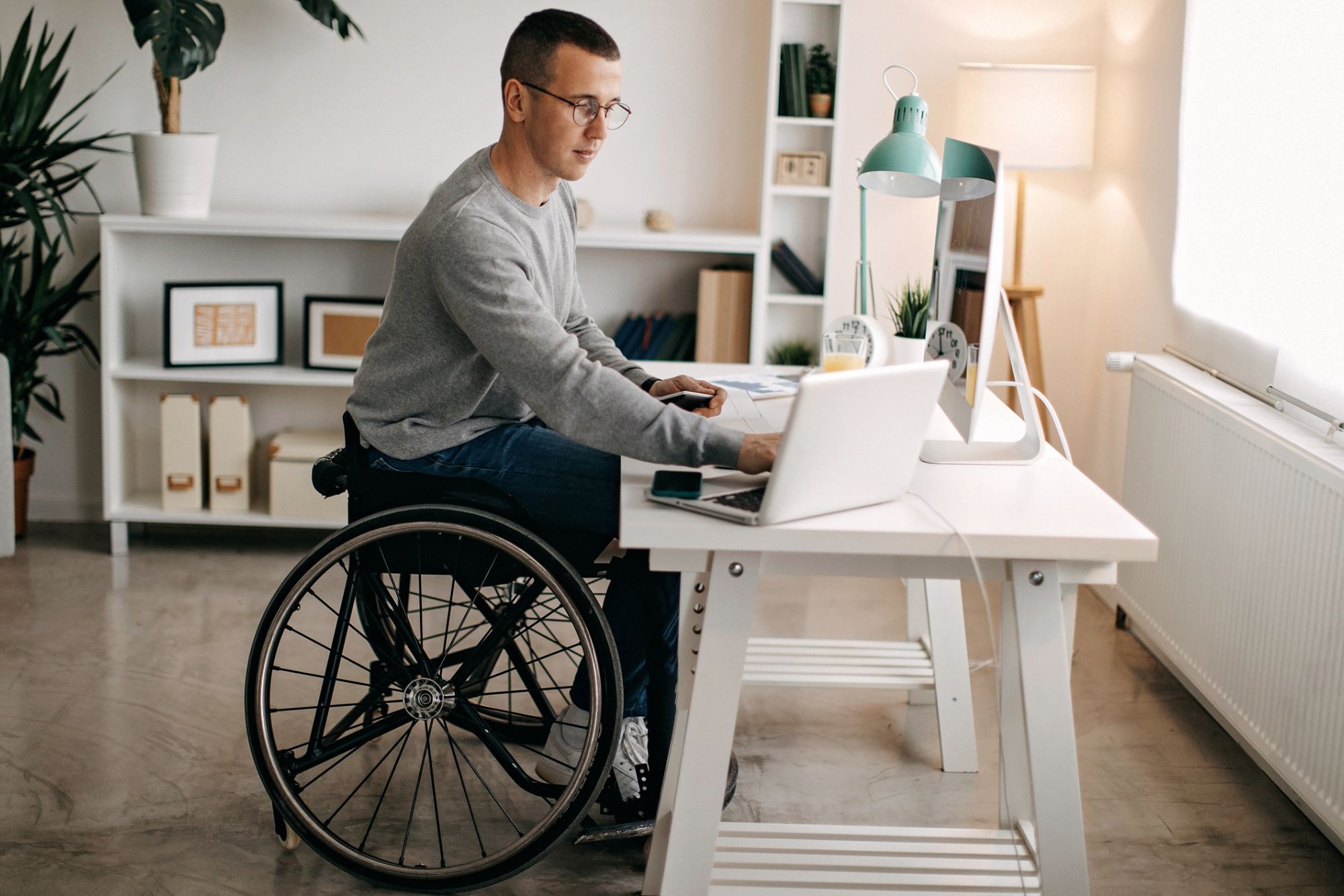 Young man digital accessibility expert in wheelchair working at desk, looking at A11Y staffing services