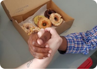 Two hands forming a handshake, with box of donuts in background for diversity, equity, and inclusion meeting